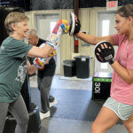 Parkinson's patient punching boxing mitts held by student.