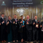 Seven honorees of Outstanding Alumni Awards Gala pose for a photo with Dean de Miranda while giving the Gig 'em thumbs up.